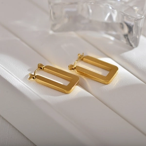 Detail of matte gold rectangular hoop earrings on white steps with glassy accents