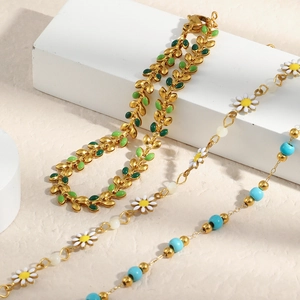 Detailed close-up of 18K gold beaded bracelets with enamel daisy and leaf charms