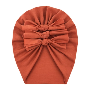 Detail of reddish-brown baby cotton turban with three decorative bows on white background