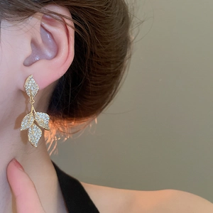 Close-up of golden leaf-shaped tassel earrings with pavé zircons worn on ear