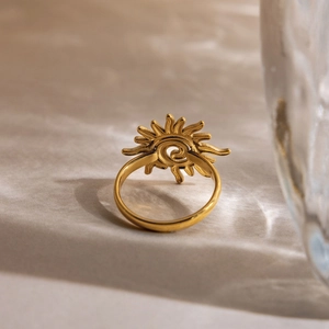 Gros plan sur la bague soleil en acier doré 18K posée sur une texture en pierre