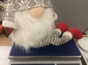 Christmas gnome topper with knitted grey hat and long white beard shown on scale for weight