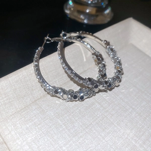 Close-up of silver geometric hoop earrings with sparkling rhinestones on a beige texture