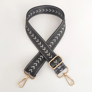 Detail of dark grey nylon shoulder strap with white arrow pattern and golden metal buckle