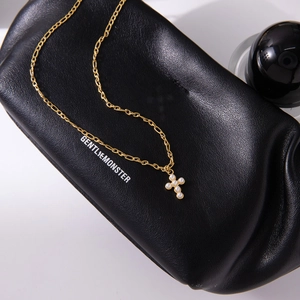 Vue détaillée d'un pendentif croix en perles dorées posé sur un étui en cuir noir