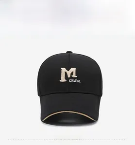Close-up of black cotton baseball cap featuring beige letter M embroidery and brim piping