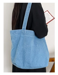 Détail du sac cabas en denim bleu avec broderie porté par un mannequin en extérieur