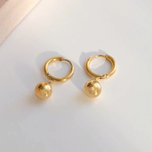 Close-up of golden hoop earrings featuring solid bead pendants on a neutral surface