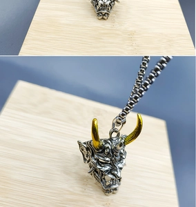 Detailed close-up of a silver Hannya mask pendant with golden horns on a steel chain