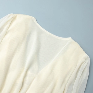 Detail of round neckline and vertical pleated chiffon texture on a cream dress