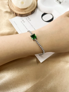 Macro shot of emerald green square zircon bracelet on wrist with gold silk background