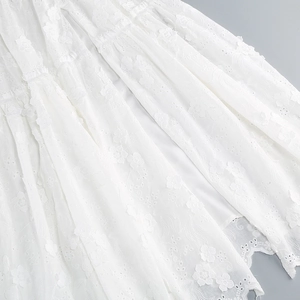 Close-up of white layered ruffle dress with intricate floral embroidery and eyelet details