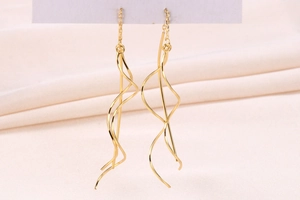 Detailed macro view of long golden spiral S925 silver threader earrings on pink fabric