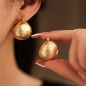 Close-up of a matte gold irregular waterdrop earring worn and held to show size and texture