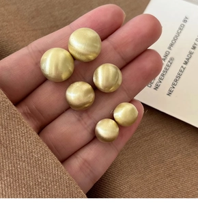 Macro shot of gold circular brushed studs in three sizes held against a warm sleeve
