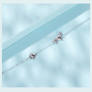 Macro detail of silver puppy and paw print charms on a delicate link bracelet