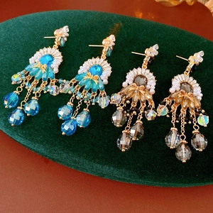 Dettaglio di orecchini vintage con perle blu e champagne su supporto in velluto verde
