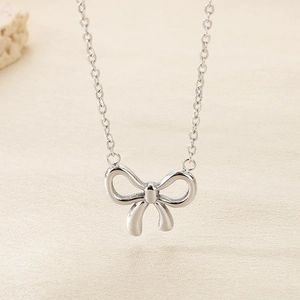 Minimalist silver stainless steel bow pendant necklace for women on beige texture
