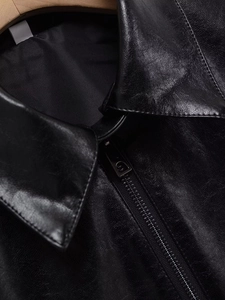 Close-up of black faux leather jacket detailing the fine texture and silver metal zipper