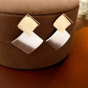 Macro shot of geometric gold and silver stud earrings with brushed metal texture
