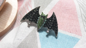 Detailed view of a bat brooch with black rhinestones and a green gem on fabric