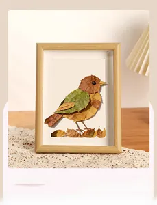 Macro shot of DIY fallen leaf bird artwork in a light wood frame on a cozy lace table