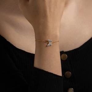 Detail of a sparkling pavé butterfly charm on a delicate gold chain bracelet worn on wrist