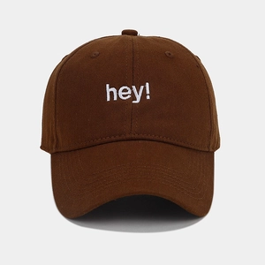 Close-up of white 'hey!' embroidery on a dark brown cotton baseball cap detail