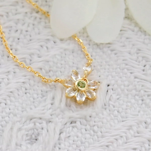 Macro detail of 14K gold floral necklace with green zircon center on white fabric