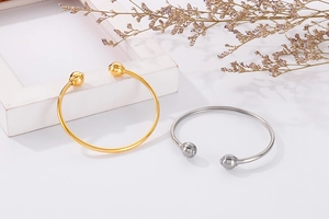 Detail shot of open metal bracelets in gold and silver with ball ends on a white surface