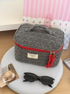 Detail of quilted checkerboard makeup bag with red zipper and top handle on tray