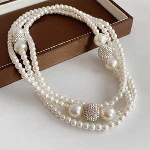 Detail of layered pearl necklace featuring sparkling rhinestone balls on white surface