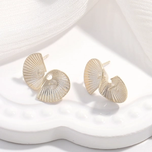 Detailed macro shot of golden spiral shell earrings with textured finish on a ceramic plate