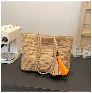 Detail of a woven straw tote bag with orange fringe tassel in a cozy coffee corner
