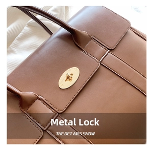 Detail of a brown leather tote with a gold oval twist lock on textured matte skin