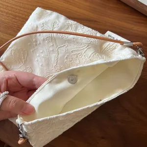 Detailed view of beige cotton linen phone bag featuring floral embroidery and magnetic clasp