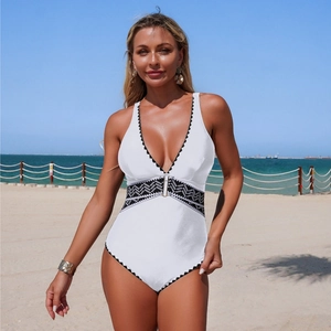 Detailed embroidery on white one-piece swimsuit with V-neckline against beach background