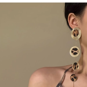 Fashionable leopard print drop earrings with gold textured circles worn by a model