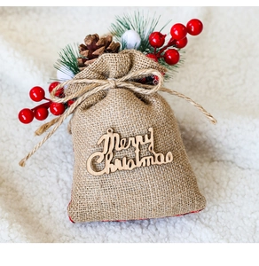 Detail of burlap Christmas gift bag with wooden Merry Christmas text and pine cone decor