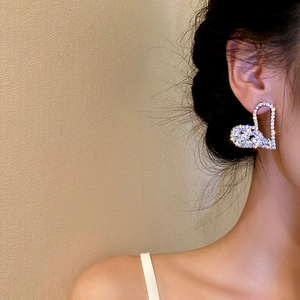 Close-up of heart-shaped silver earrings with sparkling crystals worn by a model