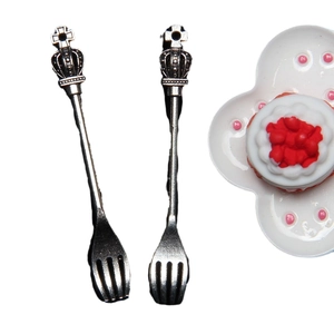 Miniature silver forks with crown design next to small dollhouse cake on white plate