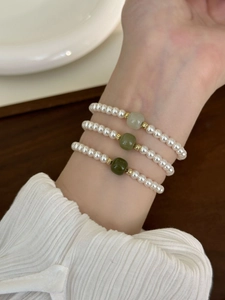 Close-up of three layered bracelets featuring white pearls, green jade, and gold beads