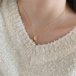 Close-up of a delicate gold knot necklace pendant worn with a beige knit sweater