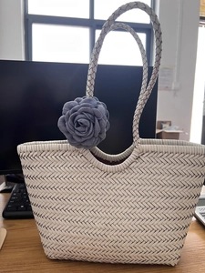 Macro detail of white woven tote bag featuring a decorative grey fabric rose charm