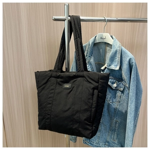 Close-up of black quilted nylon tote bag with golden logo hanging on a wooden wall