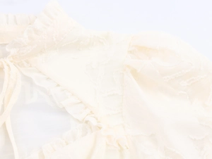 Detail of ruffled stand collar with tie-up neck on cream textured jacquard blouse