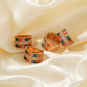 Detail of four 18K gold plated rings with colorful baguette-cut gems on satin fabric