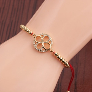 Detail of gold infinity symbol with zircon on red lucky rope bracelet worn on wrist