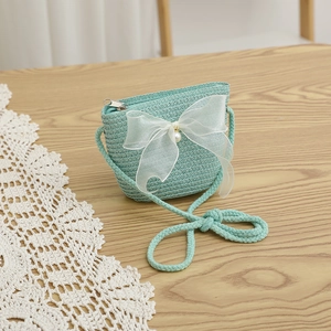 Detail of mint green straw woven purse with organza bow and pearl on wooden table