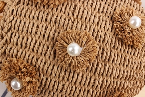 Detail of hand-woven straw bucket bag featuring raffia flowers and white pearl accents